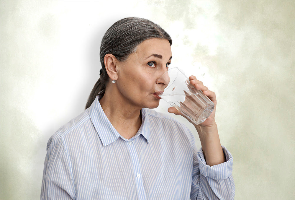 Mature woman in a striped shirt drinking a glass of water, highlighting the importance of staying hydrated for good health.