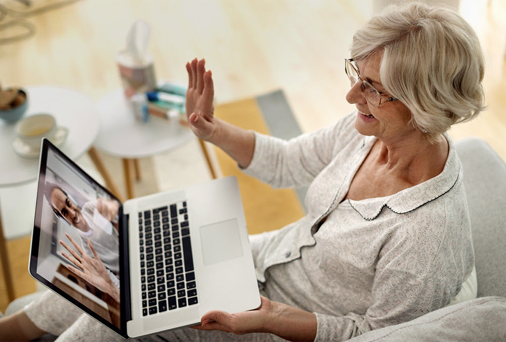 Older woman smiling and waving during a video call on her laptop, highlighting the importance of social engagement and staying connected.